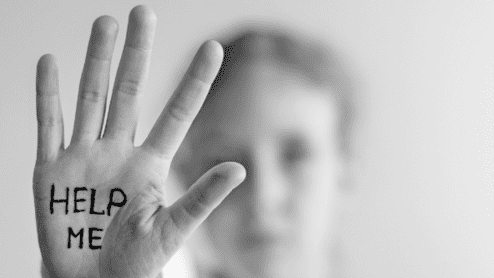 Nahaufnahme einer Hand mit der Aufschrift „HELP ME“, im Hintergrund ist eine unscharfe Person zu sehen.