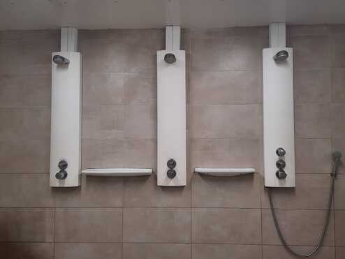 Drei Duschsäulen mit Mischbatterien und Duschköpfen an einer beigen Wandfliese installiert.