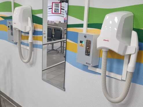 Zwei Handtrockner an einer Wand mit einem Spiegel und bunten Wandgrafiken in einem Innenraum.