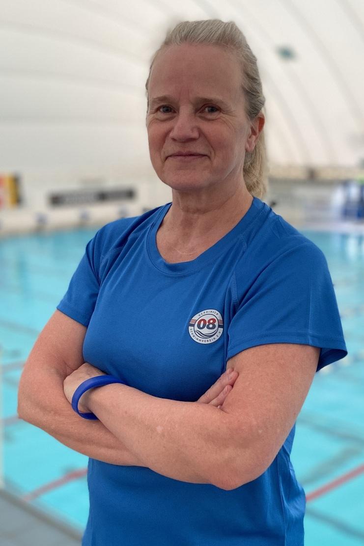 Frau in blauer Sportbekleidung steht am Beckenrand eines Schwimmbeckens mit blauer Wasseroberfläche im Hintergrund.