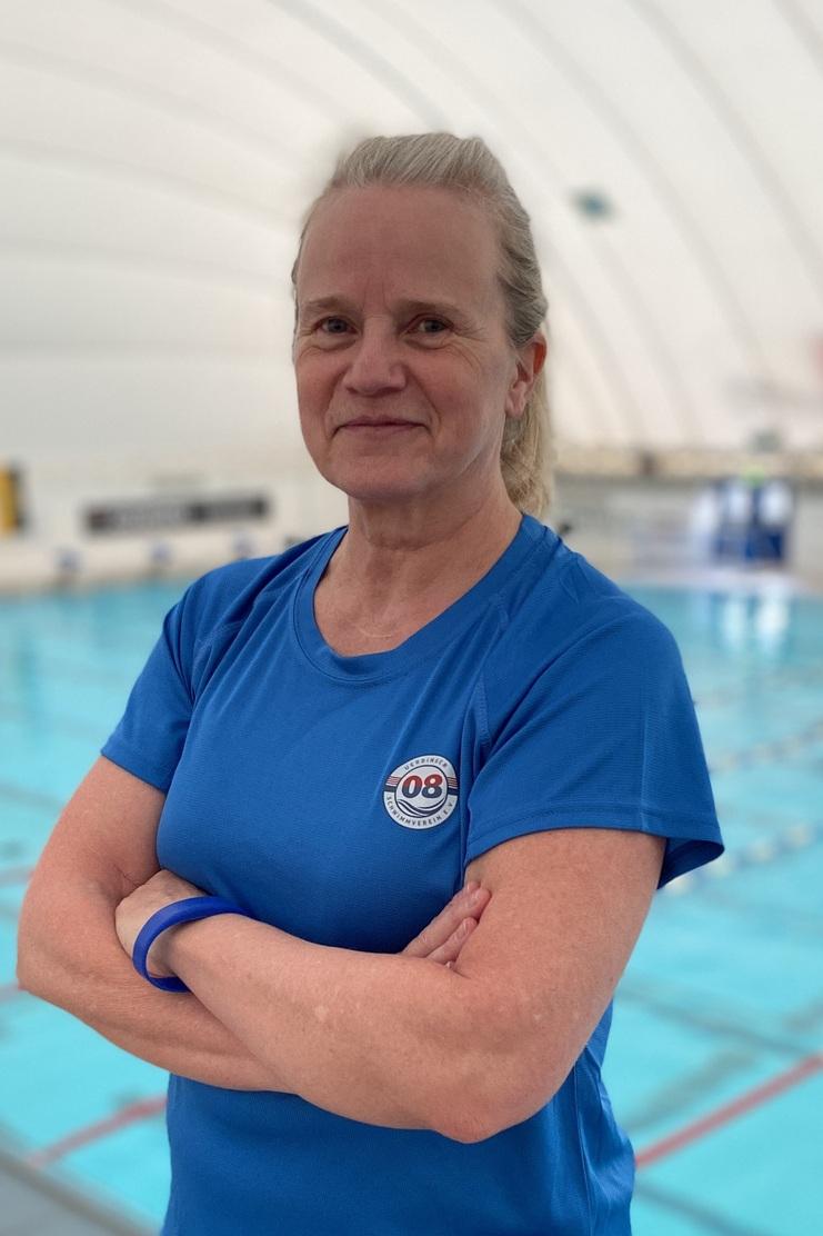 Frau in blauer Sportbekleidung steht am Beckenrand eines Schwimmbeckens mit blauer Wasseroberfläche im Hintergrund.