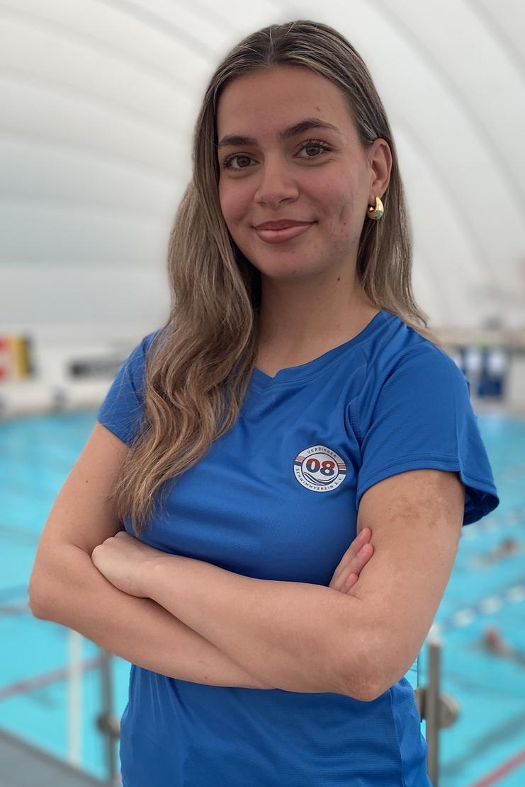 Junge Frau mit verschränkten Armen in blauer T-Shirt, Schwimmbecken im Hintergrund.