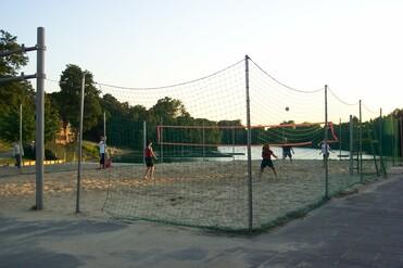 Paar Volleyballspieler auf einem Sandplatz bei Sonnenuntergang, mit einem See im Hintergrund und Netzen.