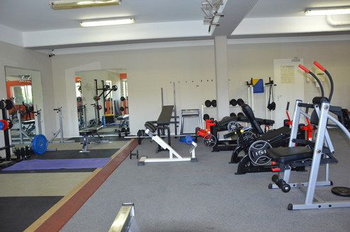 Fitnessstudio mit verschiedenen Trainingsgeräten, Gewichten und Spiegeln in einem hellen Raum.