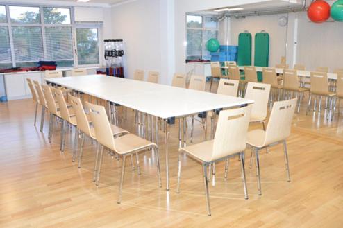 Besprechungsraum mit langer, wei&szlig;er Tafel und mehreren Holzst&uuml;hlen auf einem Holzfu&szlig;boden.