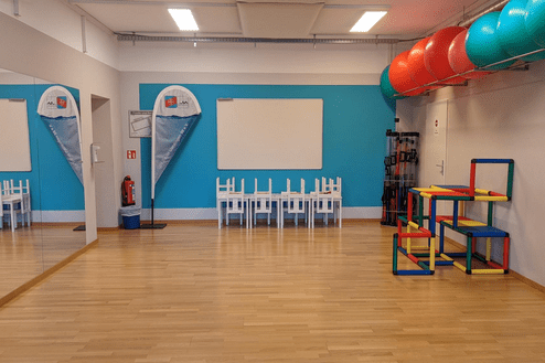 Bunte Sportger&auml;te und ein Tisch mit St&uuml;hlen in einem hellblauen Raum mit Spiegel und notes board.