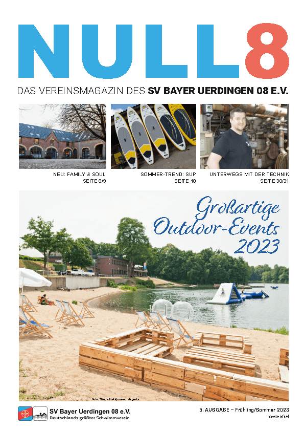 Strandabschnitt mit Liegen, einem Holzspielbereich und Stand-up-Paddle-Boards am Ufer eines Gewässers.